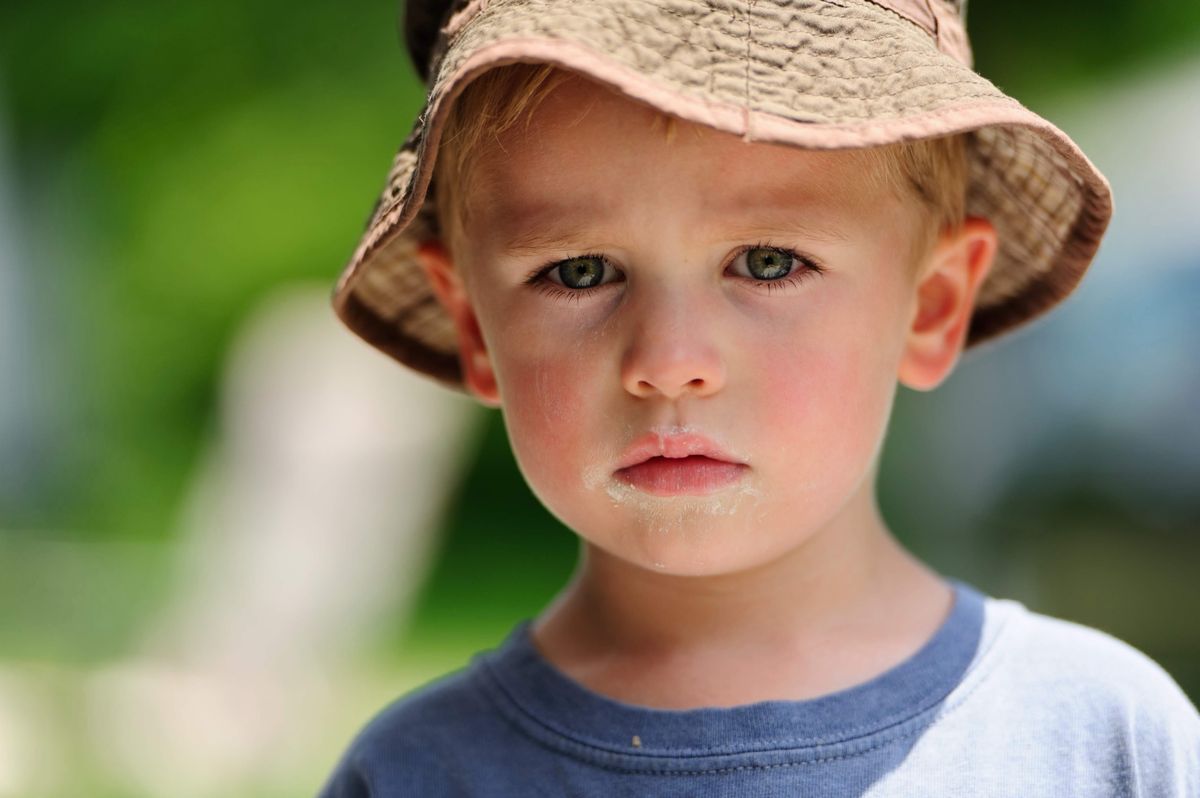 Close portrait of a small boy in a sun hat, two bright catch lights visible in his eyes