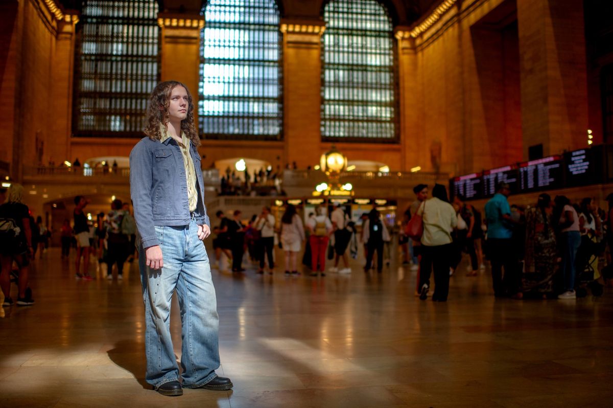 A teenage boy standing alone in the vast concourse of Grand Central Terminal, lit by a shaft of window light